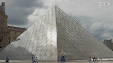 几名游客路过卢浮宫金字塔，它是卢浮宫博物馆的主要入口，也是巴黎著名的地标